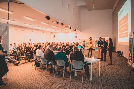 Large audience listens to 4 people giving a presentation 