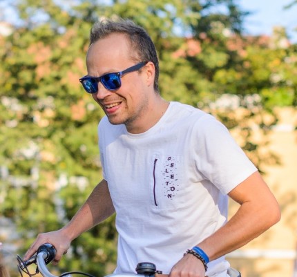 A smiling man on a bike with a white T-Shirt and blue sunglasses 